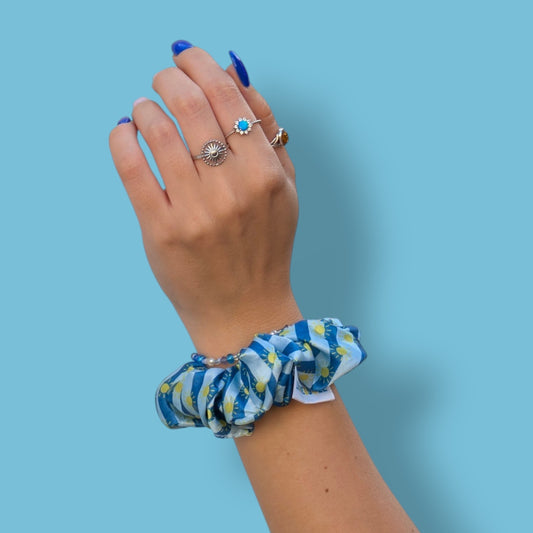 Chouchou Riviera Limone&Sole en satin bleu à rayures et motifs soleils porté au poignet d'une main manucurée