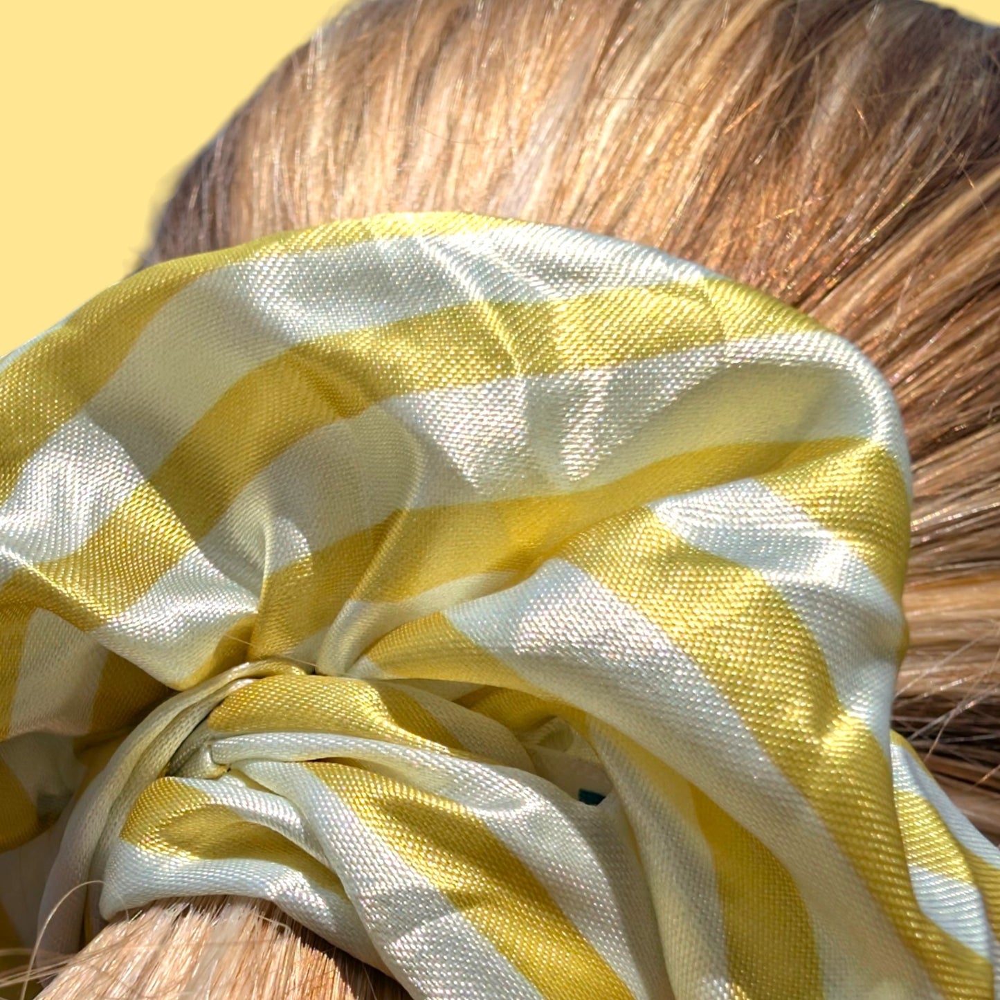 Chouchou Limone&Sole en satin rayé jaune et blanc porté dans les cheveux pour un style estival et lumineux