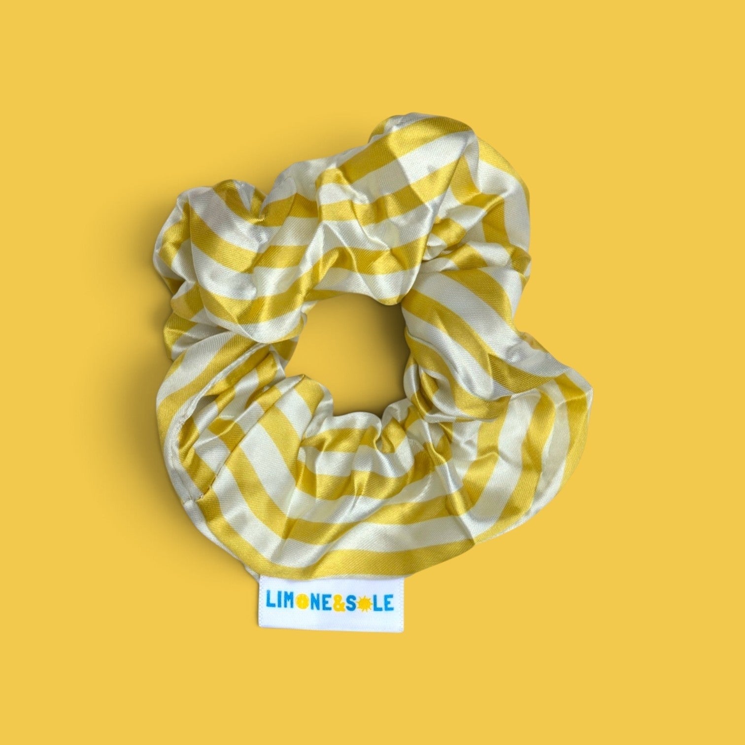 Chouchou Limone&Sole en satin rayé jaune et blanc avec étiquette tissée sur fond jaune