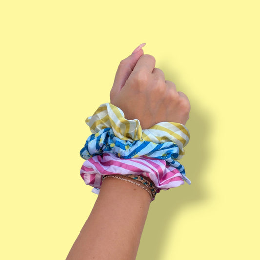 Trio de chouchous en satin Limone&Sole aux motifs rayés jaune, bleu et rose portés au poignet sur fond jaune